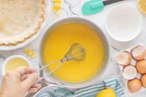 The smooth lemon mixture being whisked in a saucepan, showing the start of the bright yellow pie filling beside the pre-baked crust.