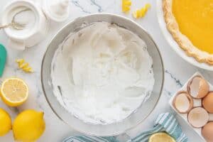 Freshly whipped meringue with soft peaks ready to be spread over the lemon filling, shown in a metal mixing bowl.