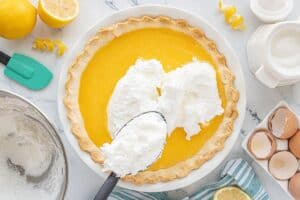 Fluffy meringue being spooned over the glossy lemon filling inside the baked pie crust, ready for baking.