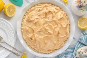 Fully baked lemon meringue pie with golden brown peaks, cooling on the counter surrounded by lemons and dessert plates.