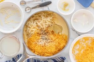 A pan filled with shredded cheese, Dijon mustard, seasonings, and shredded cheese on a marble counter.