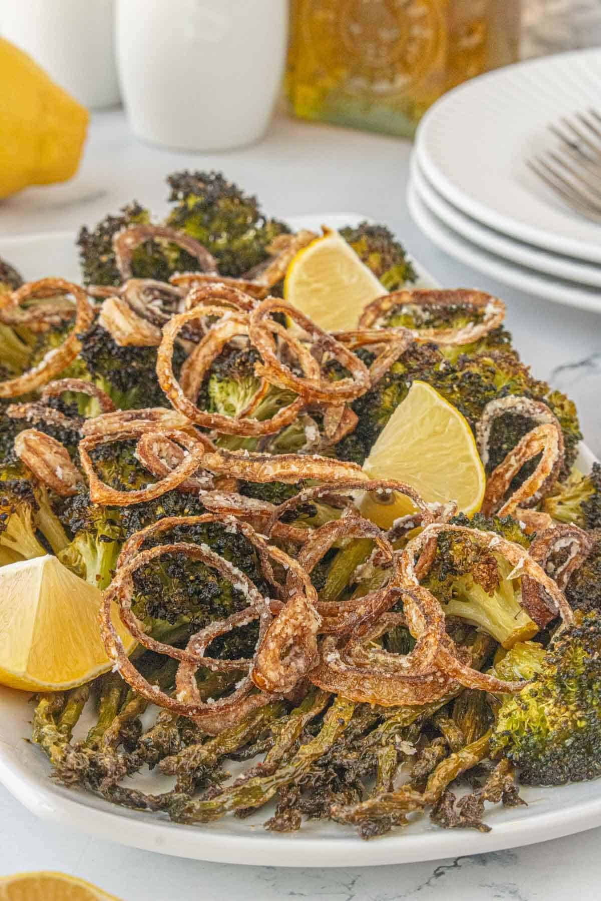 Close-up of roasted broccoli and asparagus topped with crispy fried shallots and lemon wedges on a white serving plate.