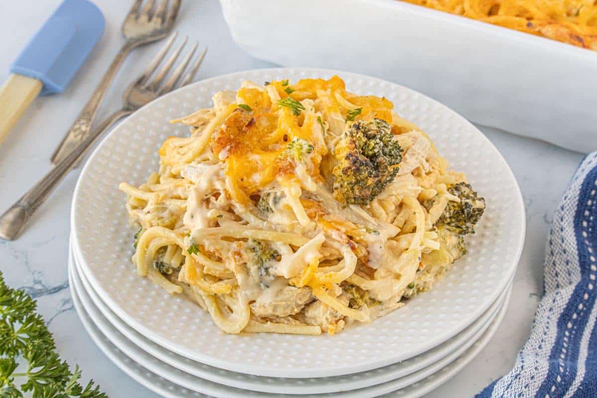 A serving of creamy broccoli chicken spaghetti bake on a white plate, topped with melted cheddar cheese and garnished with parsley.