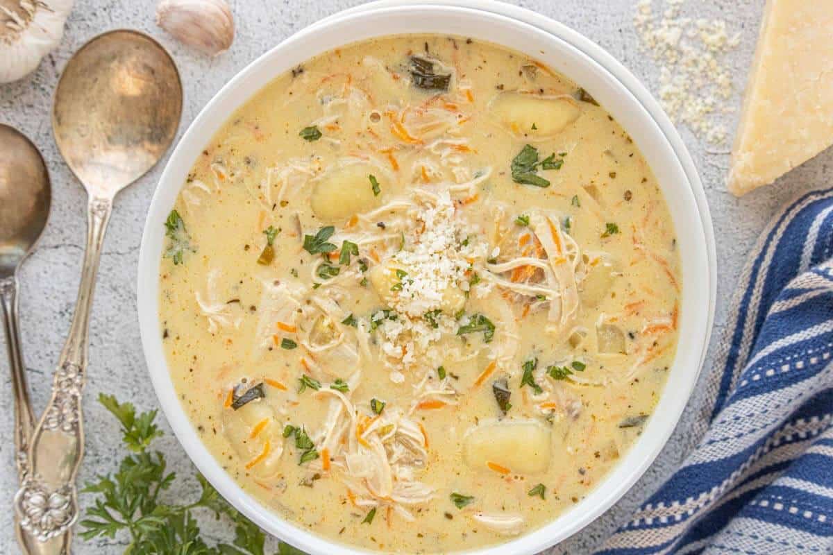 Bowl of chicken gnocchi soup garnished with shredded cheese and parsley, ready to serve.