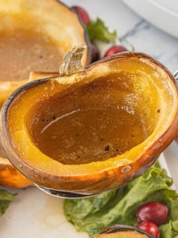 Close-up of a caramelized acorn squash half being lifted from a serving platter, showing the glossy brown sugar butter mixture inside.