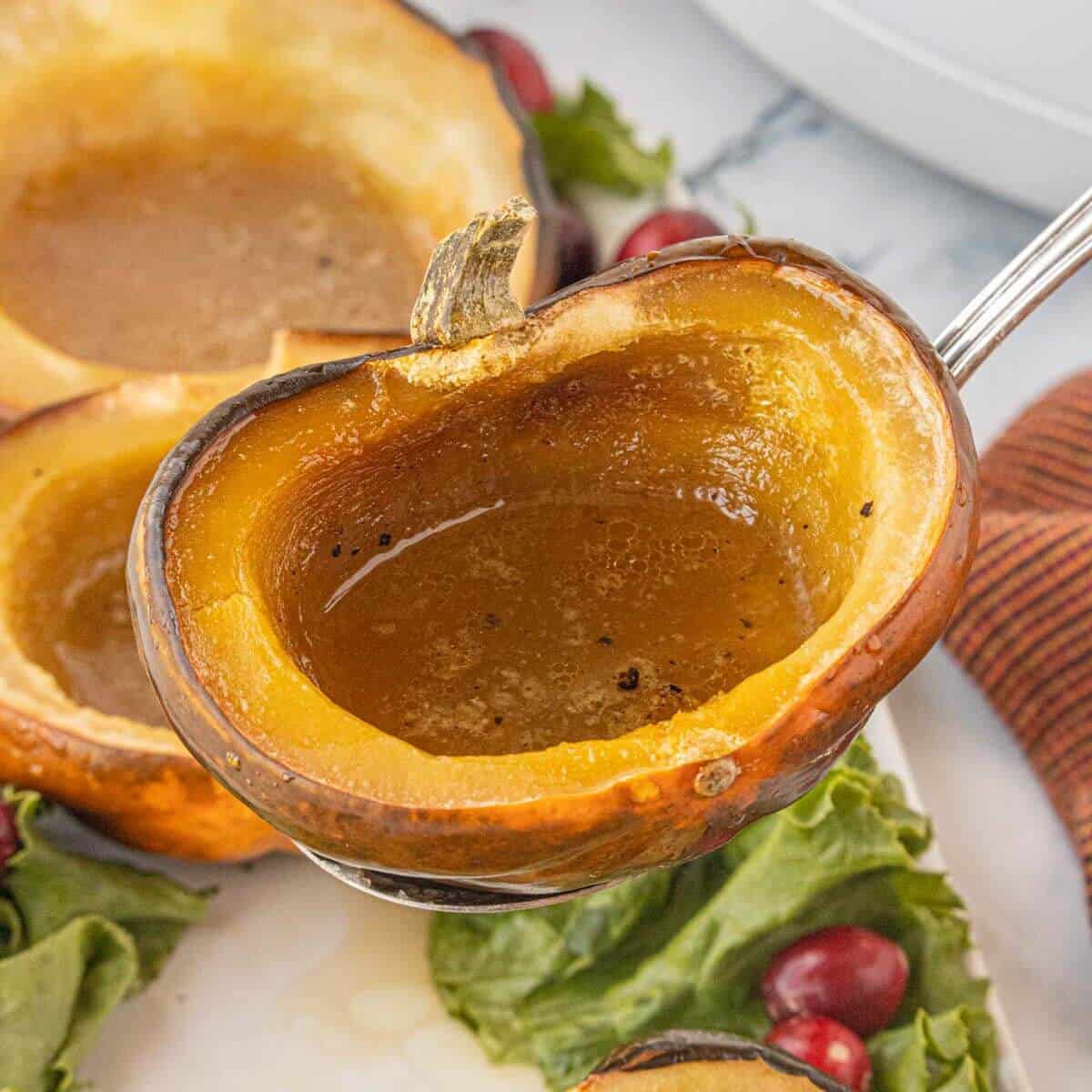 Close-up of a caramelized acorn squash half being lifted from a serving platter, showing the glossy brown sugar butter mixture inside.