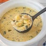 Ladle lifting a hearty scoop of creamy chicken gnocchi soup with shredded chicken, gnocchi, and spinach.