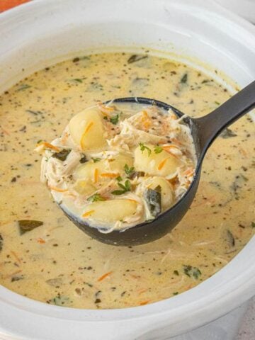 Ladle lifting a hearty scoop of creamy chicken gnocchi soup with shredded chicken, gnocchi, and spinach.