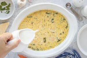Hand pouring milk into the crockpot of creamy chicken gnocchi soup before the final stir.