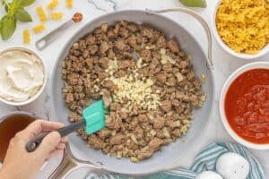 Cooking ground beef and sausage with onions and minced garlic in a skillet.