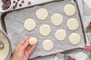 A parchment-lined baking sheet with round peppermint filling discs being shaped and arranged by hand, ready for chilling before dipping in chocolate.