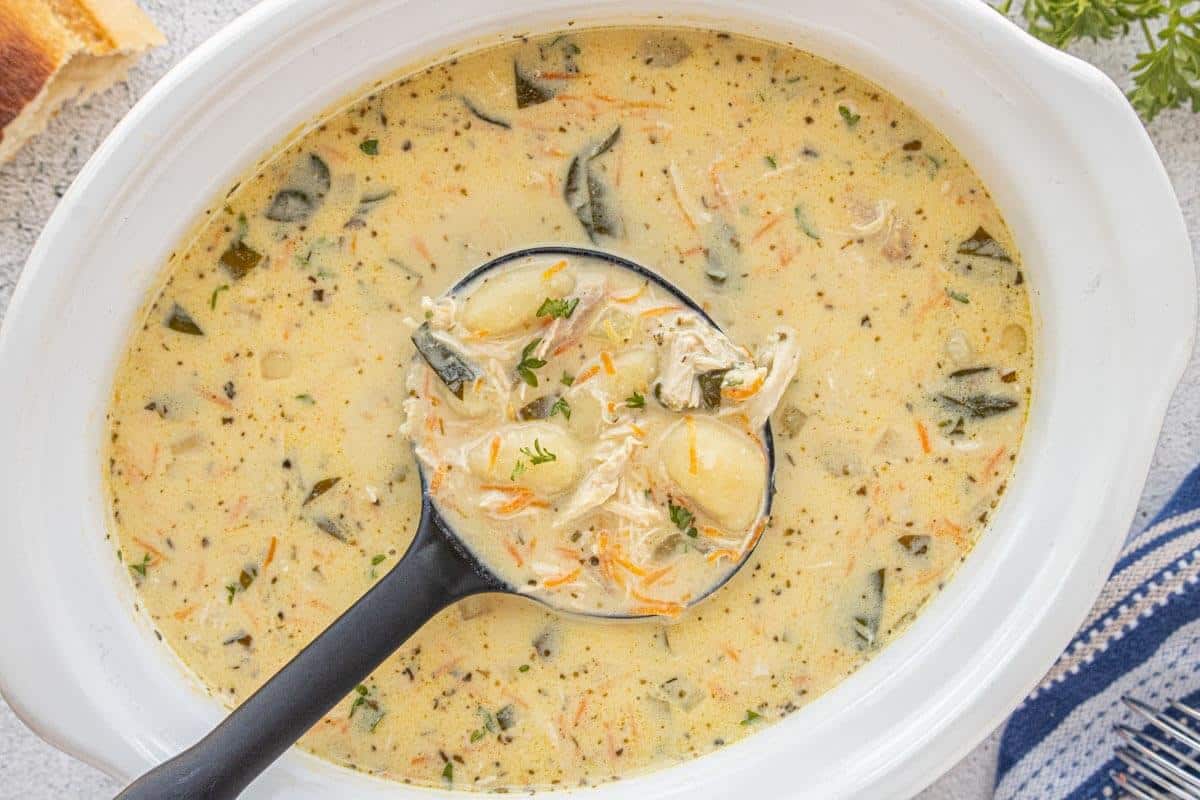 Overhead view of crockpot filled with chicken gnocchi soup, showing tender gnocchi, shredded chicken, and spinach in a rich, creamy broth.
