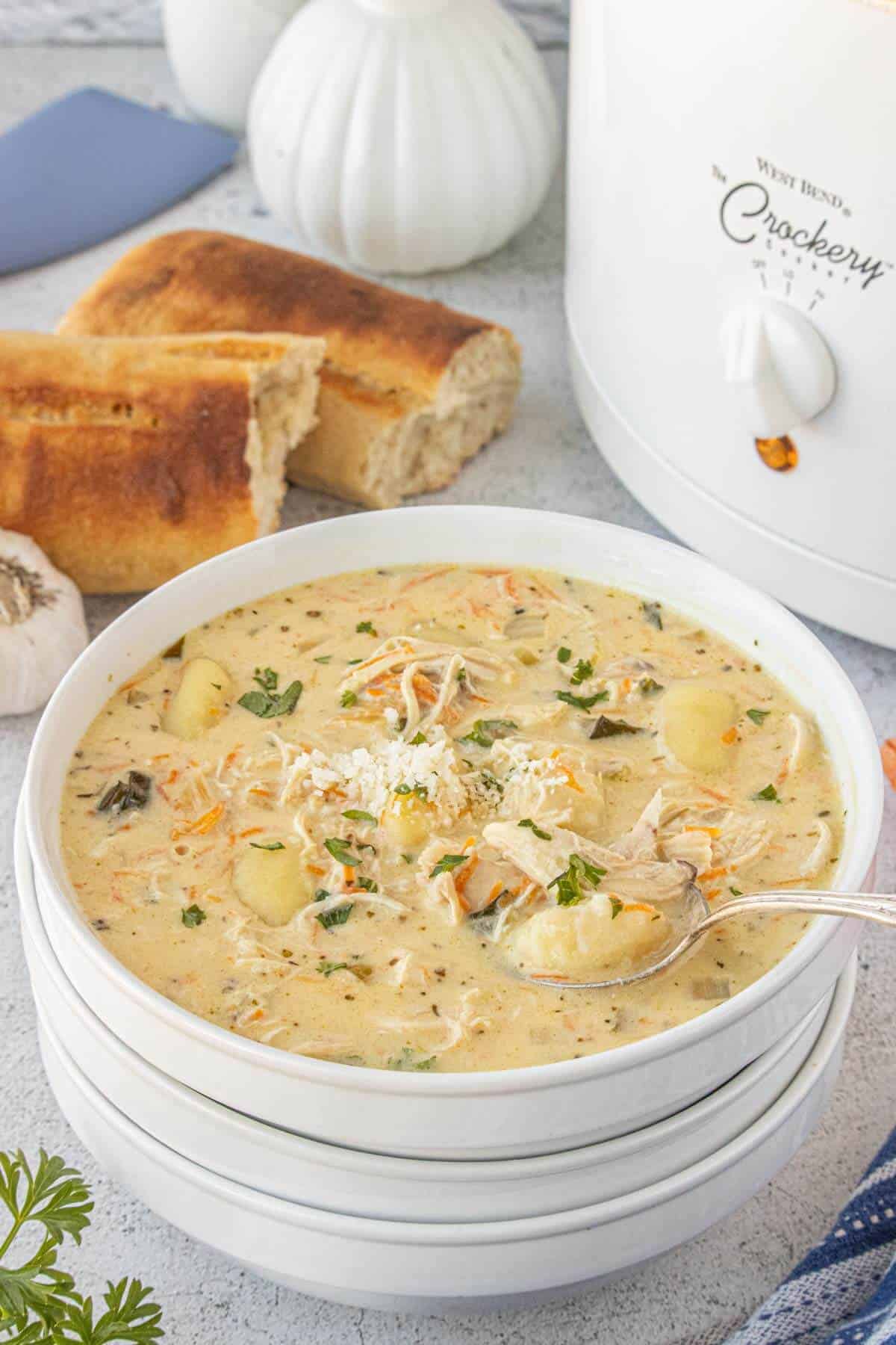 Bowl of chicken gnocchi soup served with toasted bread and a slow cooker in the background.