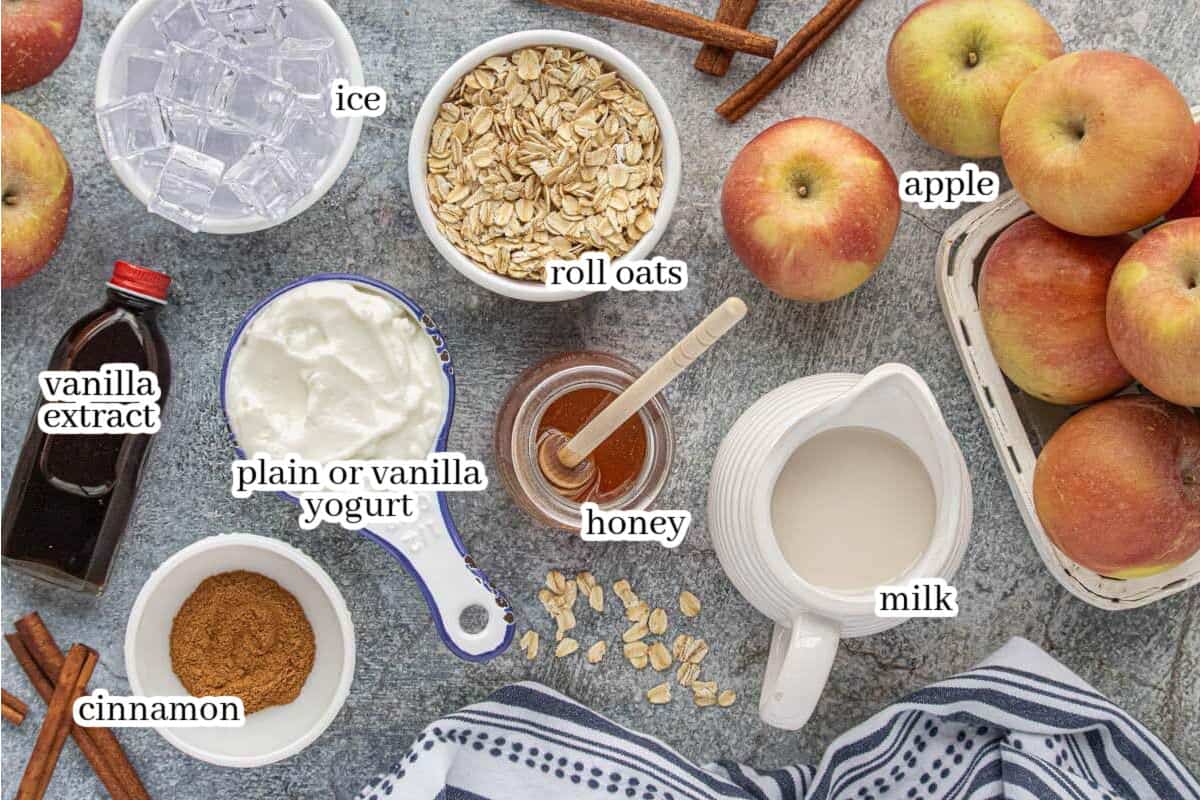 All of the ingredients to make the smoothie recipe, including apple, milk, oats, honey, cinnamon, yogurt, vanilla extract and ice. With print overlay for clarification.
