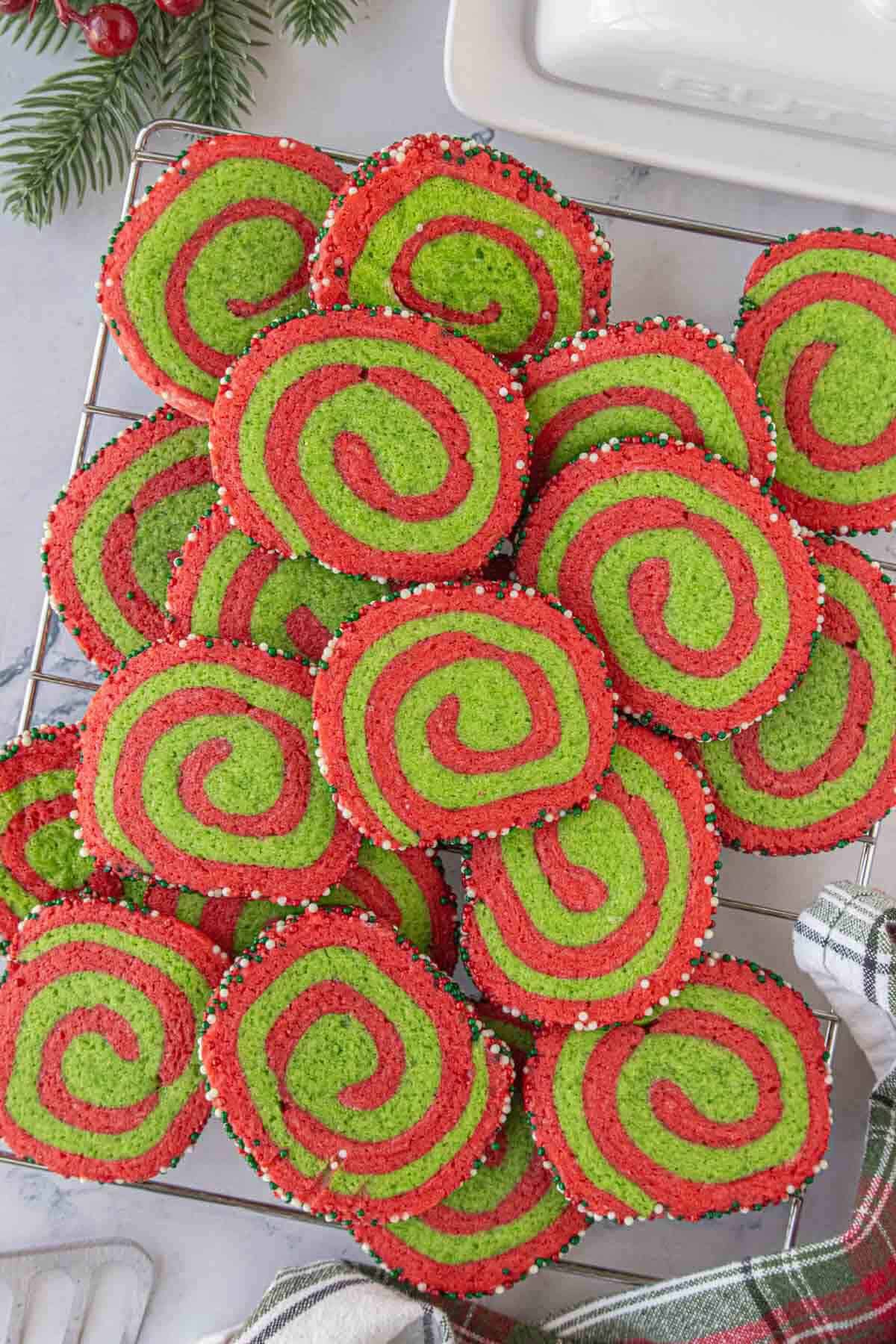 A cooling rack filled with colorful red and green pinwheel cookies arranged in a large overlapping pile.