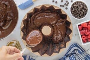 Thick chocolate batter being spooned into a greased Bundt pan dusted with cocoa powder.