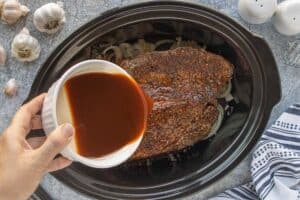 Beef roast in a slow cooker as a rich broth is poured over the top.