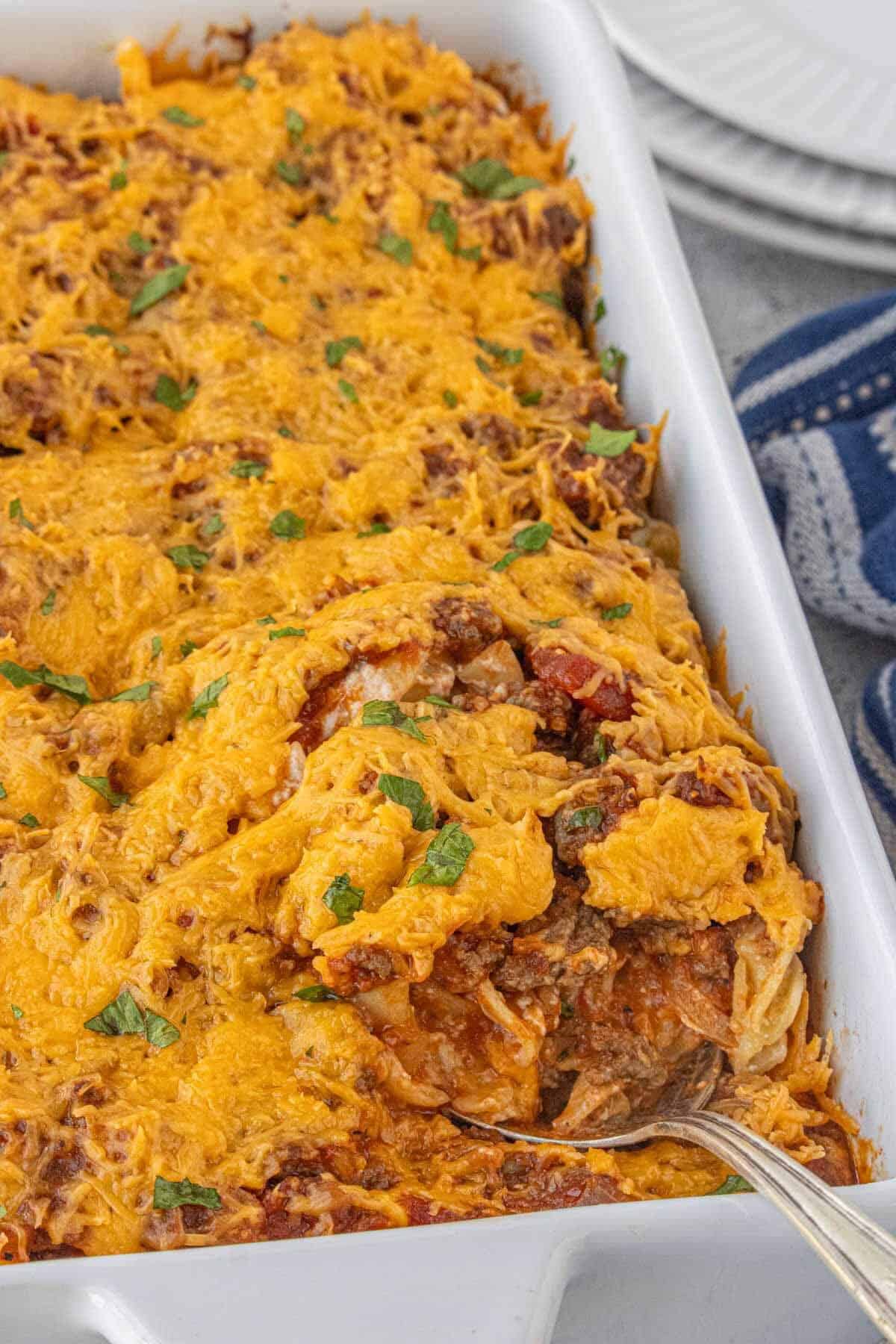 Full baking dish of cheesy casserole with browned edges and a serving spoon resting inside.