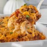 Close-up of a cheesy casserole scoop with noodles, beef, and sauce on a serving spoon.