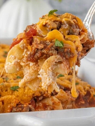 Close-up of a cheesy casserole scoop with noodles, beef, and sauce on a serving spoon.