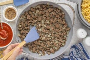 Ground beef and diced onions cooking together in a large skillet, stirred with a silicone spatula.