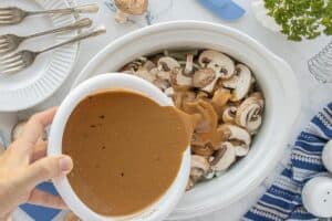 Gravy mixture being poured over meatballs, onions, and mushrooms in the slow cooker.