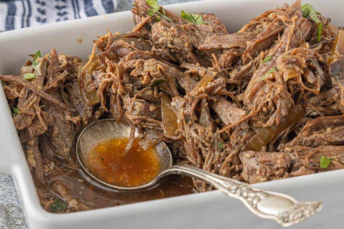 Shredded beef in a serving dish with a ladle scooping up the savory broth.