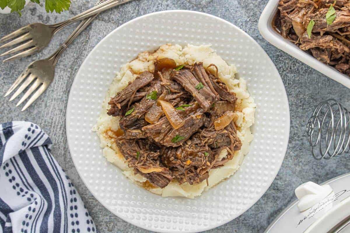 Shredded beef served over mashed potatoes on a white plate.