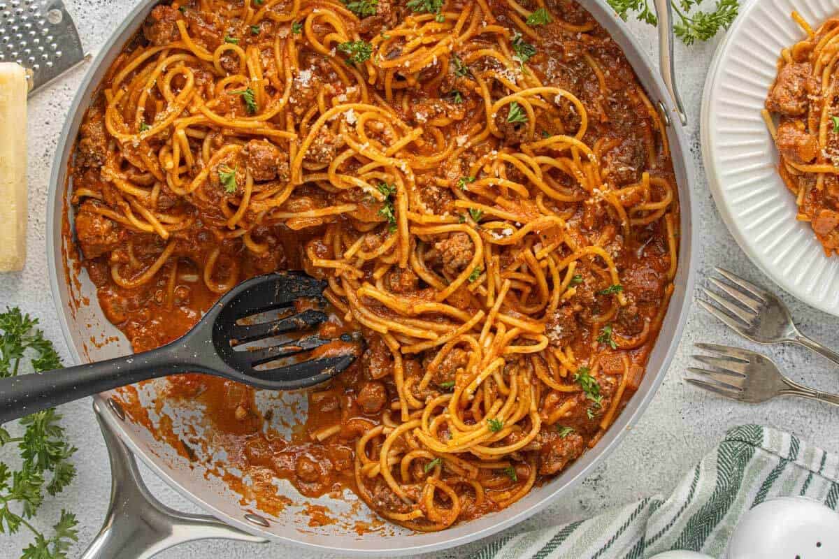 Overhead view of spaghetti hamburger helper cooking in a skillet with pasta, meat sauce, and parsley garnish.