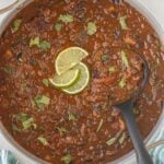 Overhead view of pot of chili with a ladle for serving, garnished with fresh herbs and lime slices.