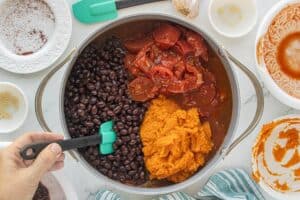 Black beans, pumpkin puree, and stewed tomatoes added to browned turkey and vegetables in a large pot.