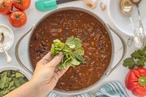 Adding chopped spinach to turkey veggie chili during the final stage of simmering.