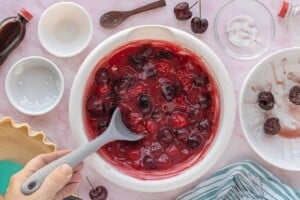 Cherry pie filling fully mixed in a bowl, showing thickened juices and whole cherries before adding to the crust.