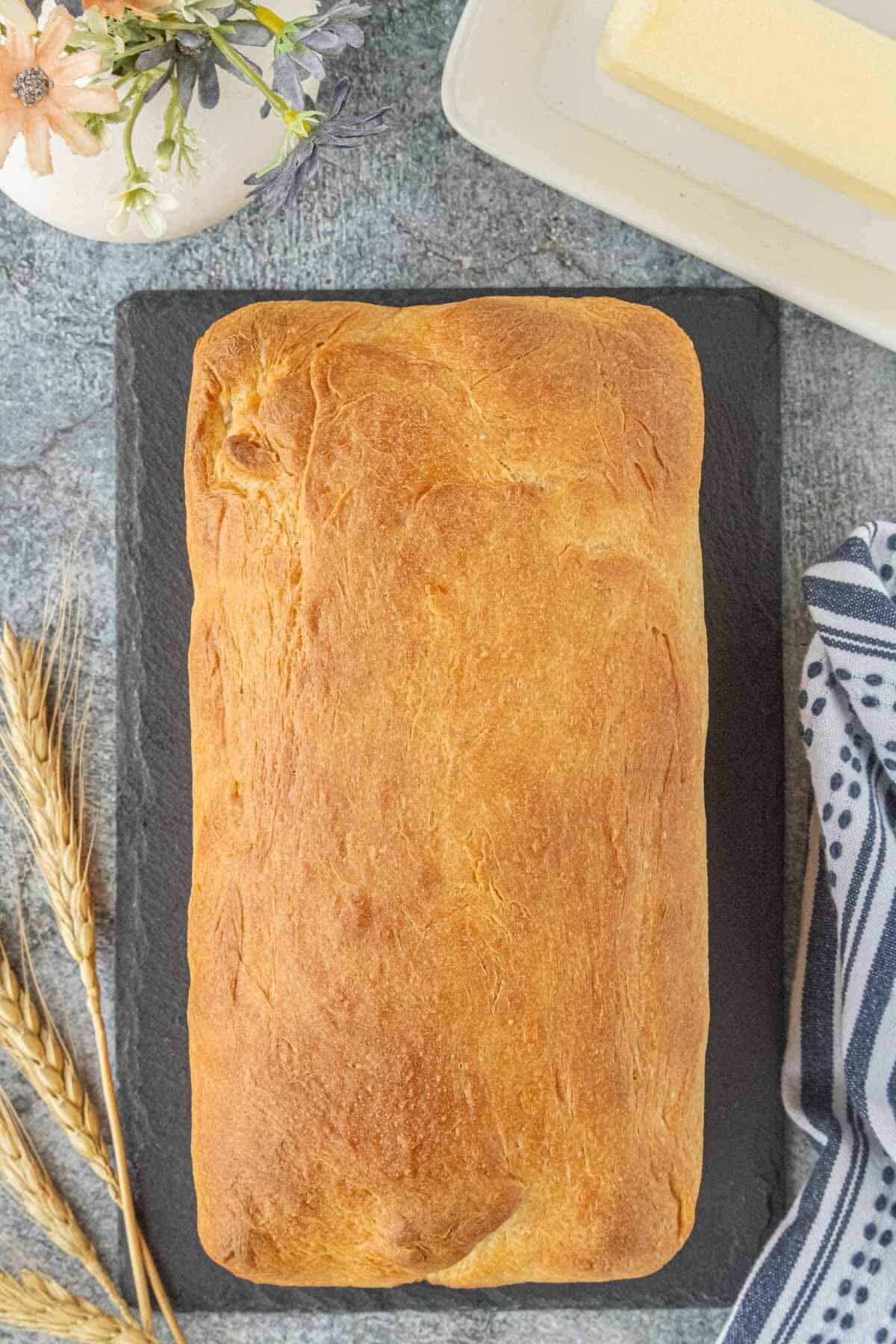 Golden brown sandwich bread loaf resting on a slate board after baking.