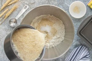 Foamy yeast mixture being poured into a mixing bowl with flour, salt, and vital wheat gluten for soft sandwich bread.