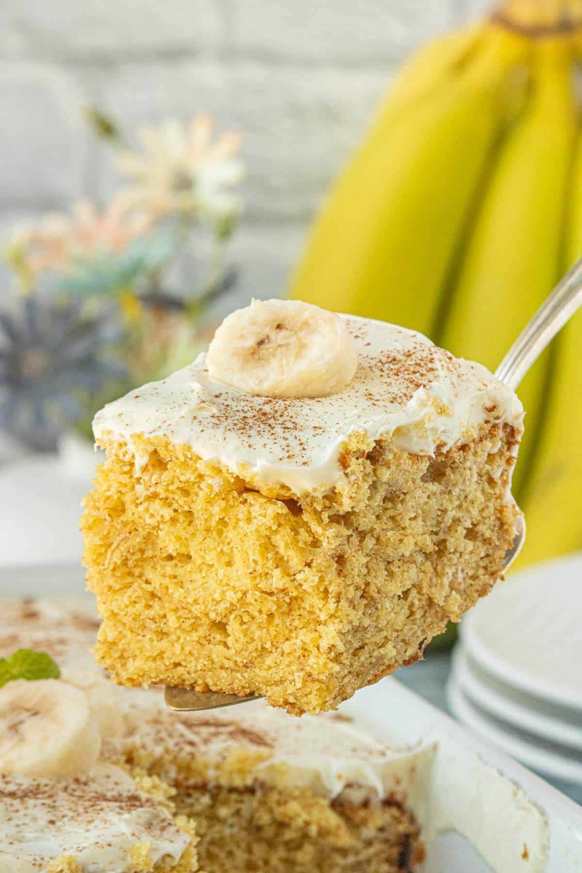 Thick slice of banana cake with frosting and a banana slice on top.