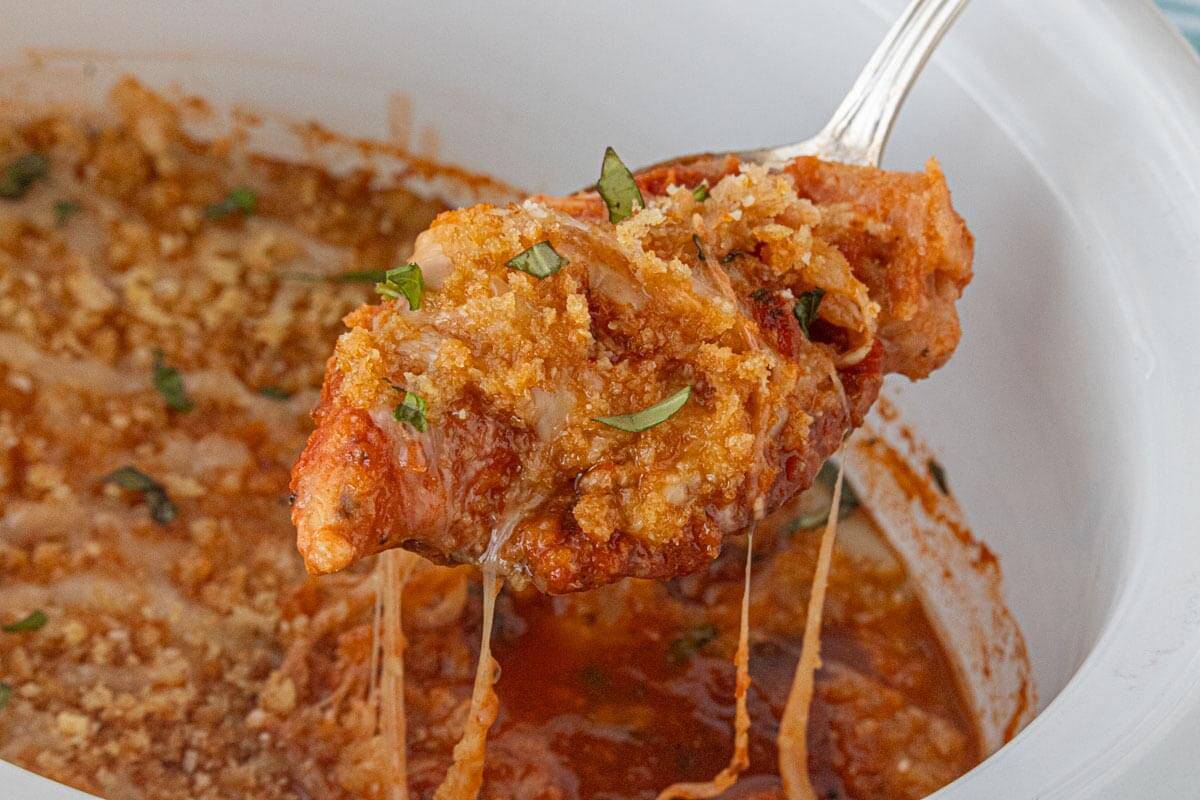 Golden chicken parmesan being lifted from a crockpot with a serving spatula.