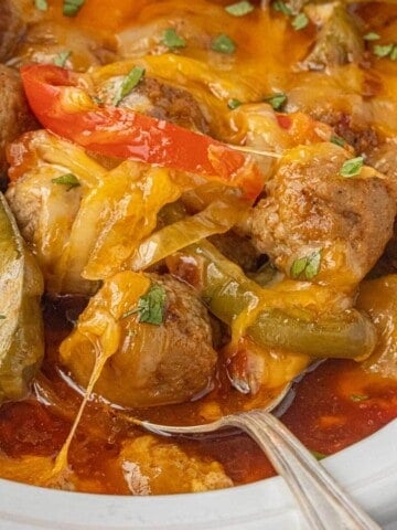 Slow cooker filled with saucy Burrito meatballs, with peppers, onions, and topped with melted cheese.