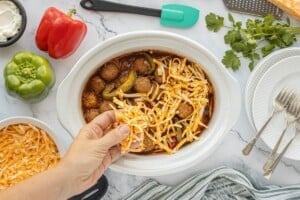 Hand sprinkling shredded cheese over meatballs in the slow cooker before serving.