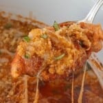 Close-up of tender chicken with melted cheese and crunchy breadcrumb topping, held with a spoon.