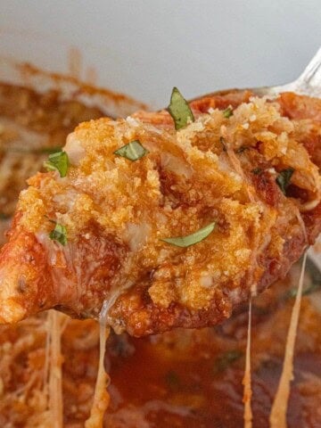 Close-up of tender chicken with melted cheese and crunchy breadcrumb topping, held with a spoon.