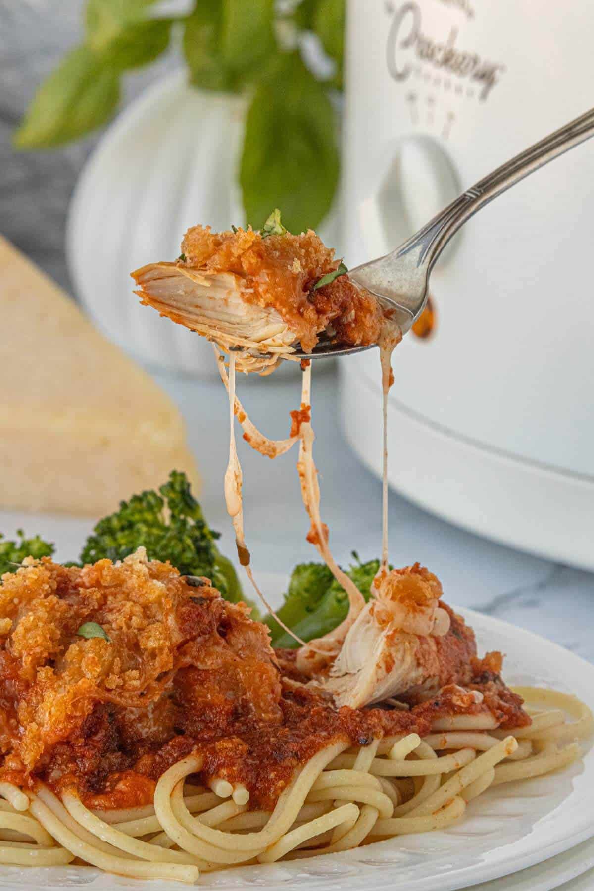 Chicken parmesan served over spaghetti. A fork is lifting a cheese bite of tender chicken.