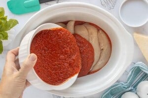 Raw chicken tenders layered in a slow cooker with pasta sauce spread underneath.