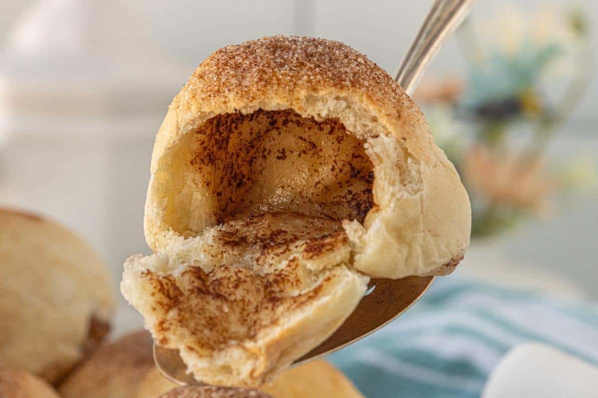 Close-up of a baked roll broken open on a spoon, showing the hollow center and cinnamon-sugar interior of the resurrection roll.
