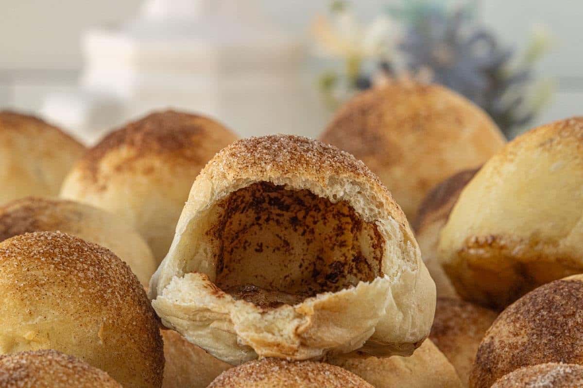 A platter of Resurrections rolls with one roll opened to reveal the empty center, surrounded by freshly baked rolls on a cooling rack.