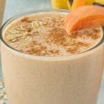 Glass of peach smoothie topped with oats and cinnamon and garnished with a peach slice, with text overlay reading “Peach Pie Smoothie Recipe.”