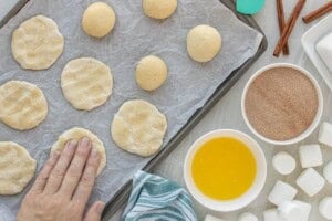 Hand pressing thawed dough into flat circles on a parchment-lined sheet pan.