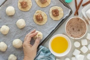 Cinnamon sugar-coated marshmallow placed in the center of flattened dough with hand sealing dough around a marshmallow filled roll.