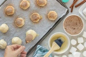 Shaped dough balls brushed with melted butter and sprinkled with cinnamon sugar before baking.