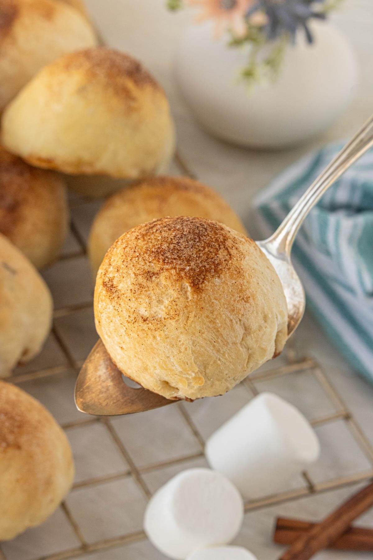 Golden baked empty tomb roll with cinnamon sugar topping resting on a spoon above a cooling rack.